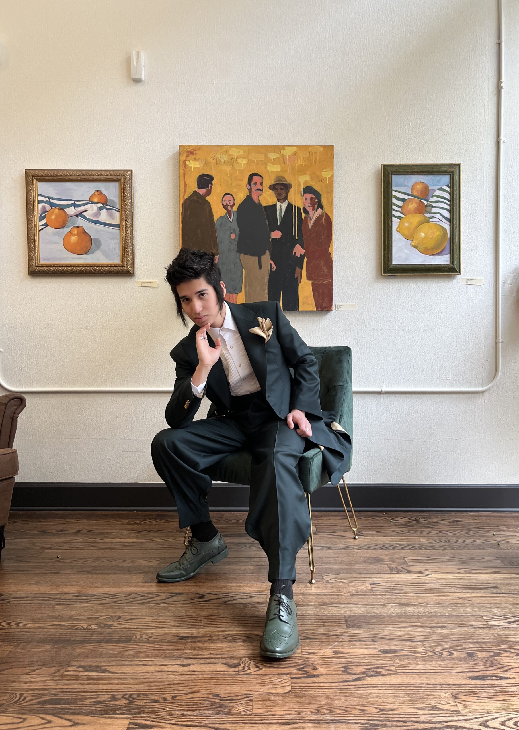 man wearing a zoot suit posed against a gallery wall 